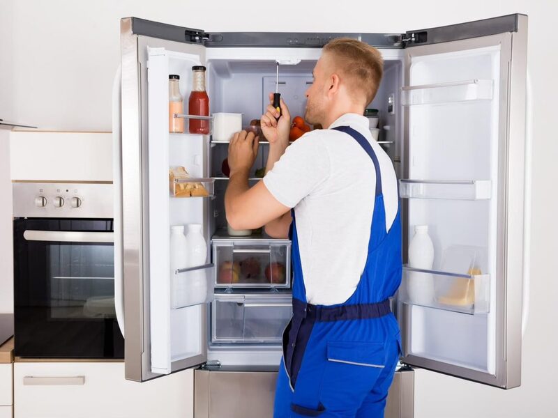 Technician repairing an open French door refrigerator in a kitchen